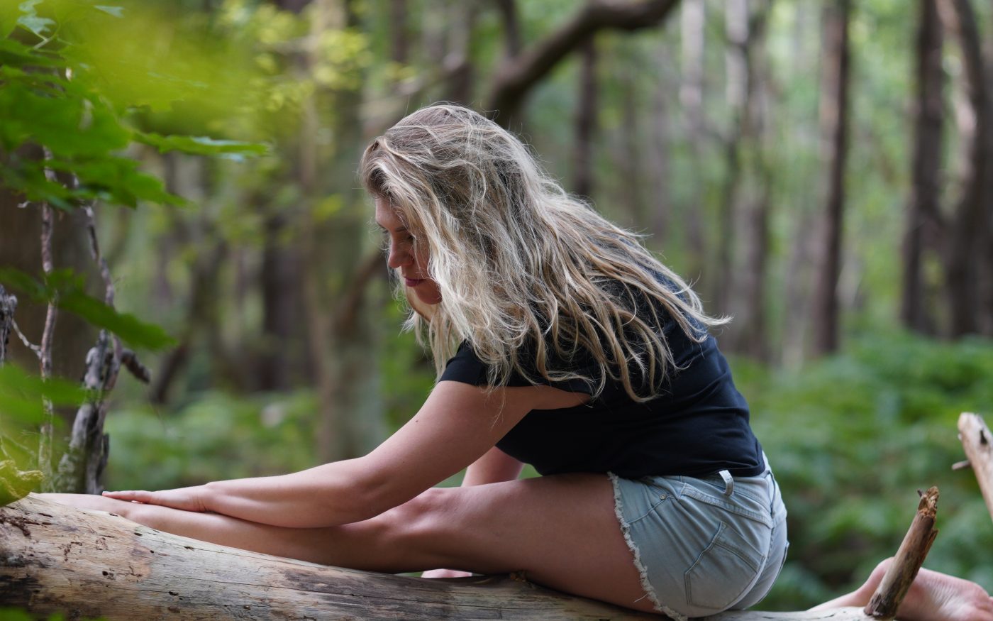 Hanne in een yogahouding op een omgevallen boom in het bos